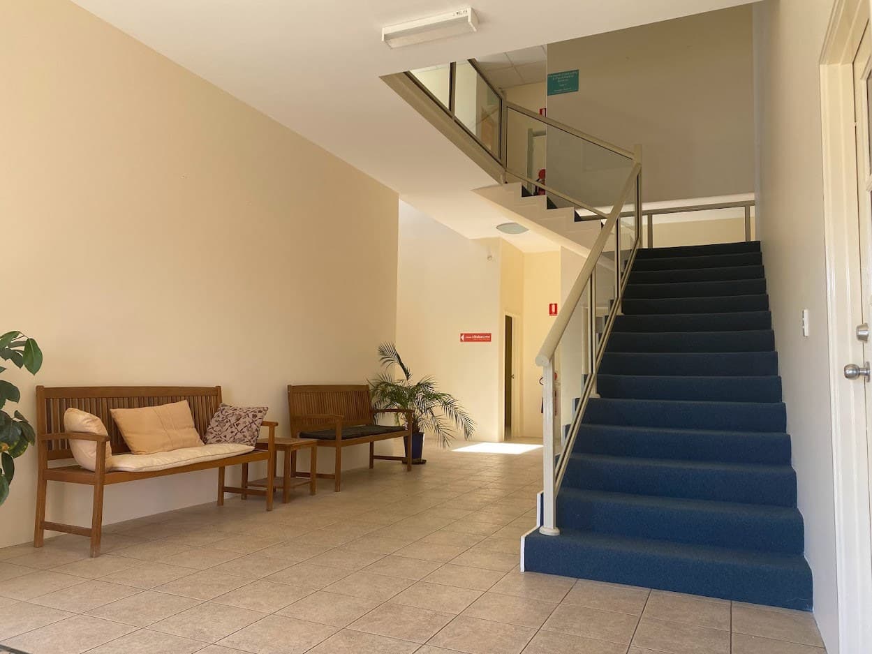 Painted office lobby with timber benches and a blue-carpet stair