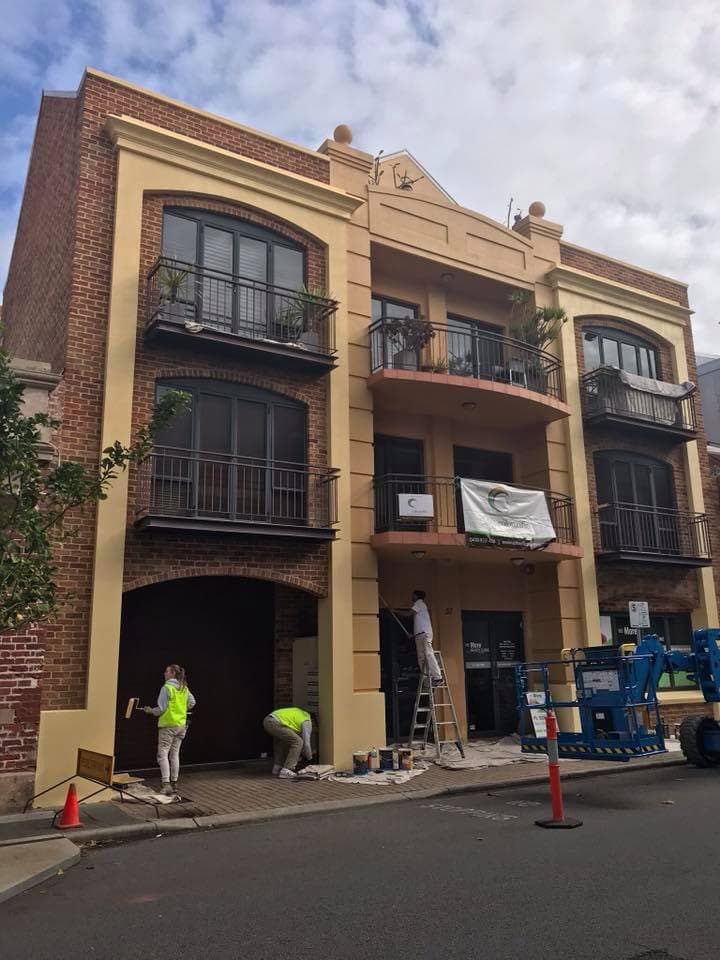 Painters and a cherry picker on a cream-and-brick apartment exterior