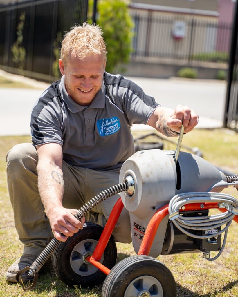 Frank of Frank Britton Plumbing kneeling on a lawn with a RIDGID drain machine