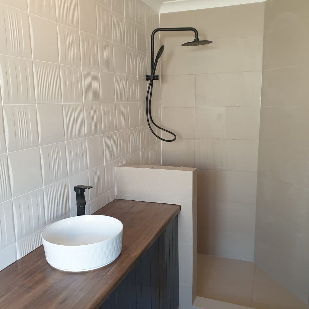 Walk-in shower with black overhead rose and a vessel basin on a timber benchtop