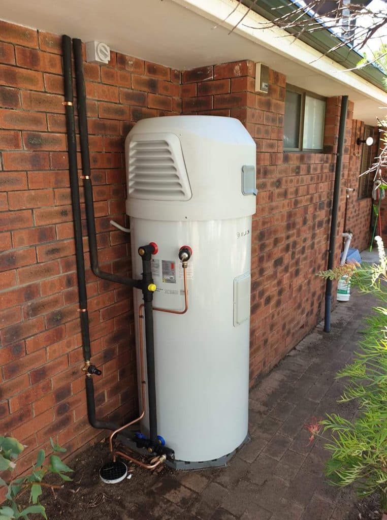 Storage hot water cylinder installed against a brick house wall