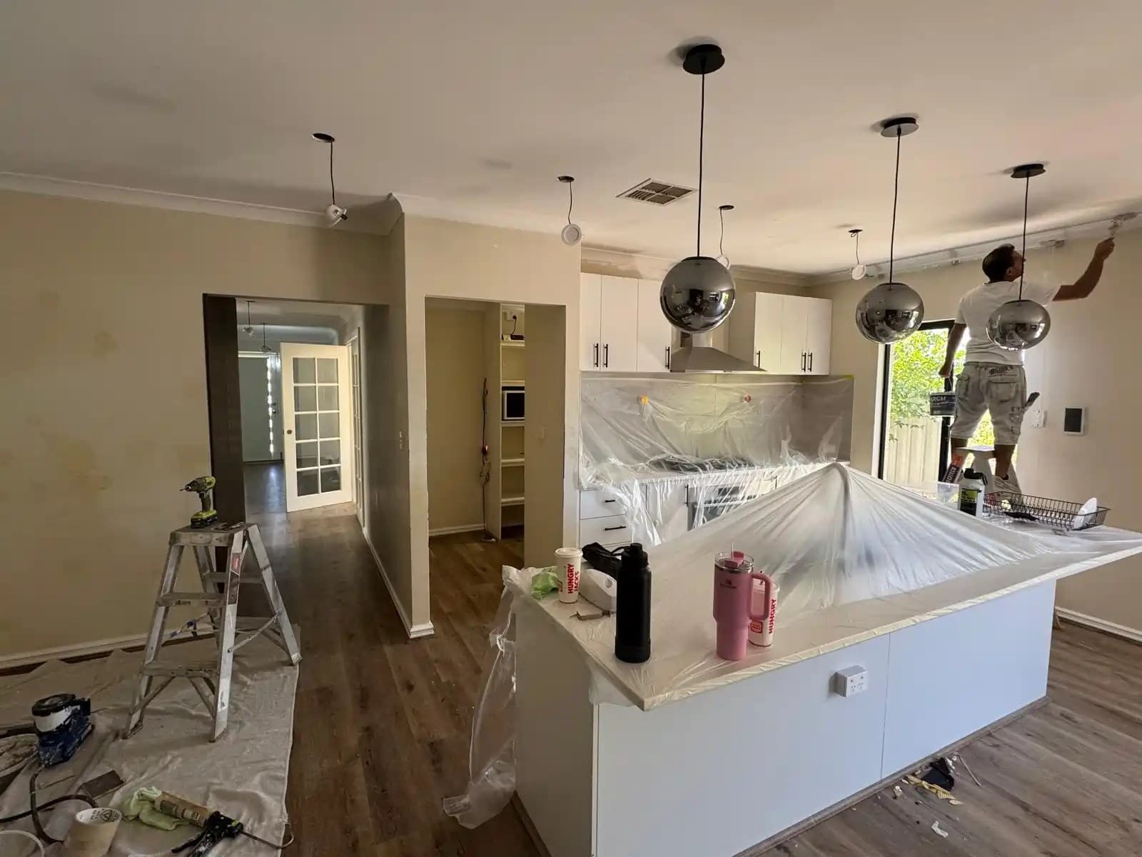 Painter cutting in a kitchen ceiling, island bench covered in plastic