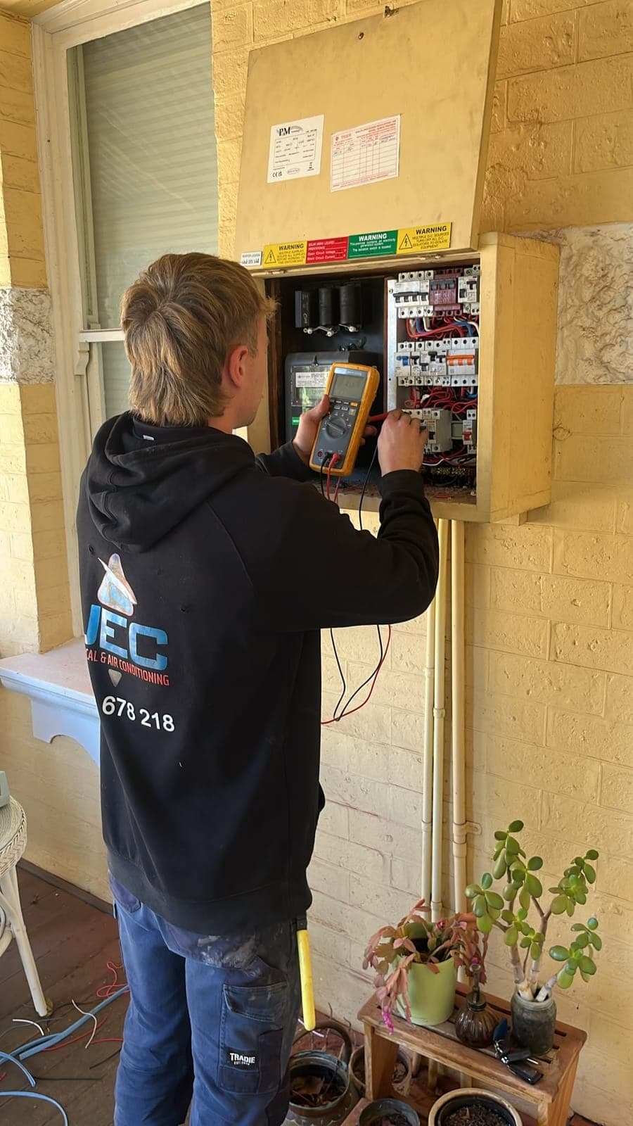 JEC electrician testing a switchboard with a multimeter