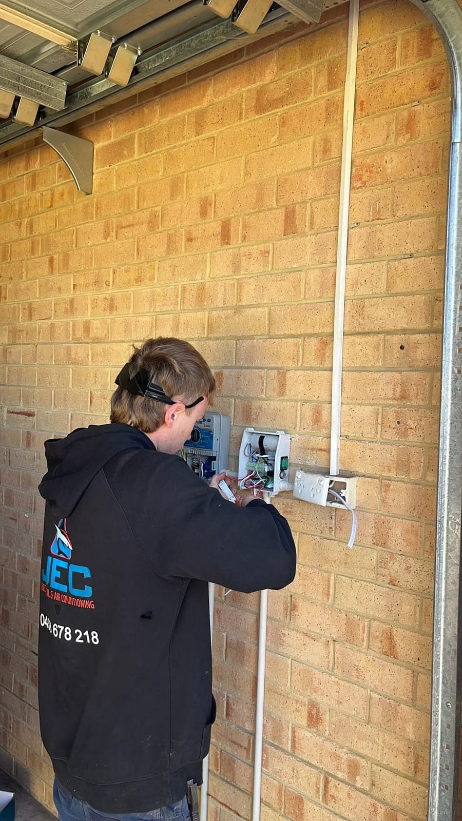 JEC electrician wiring a box on a cream brick garage wall