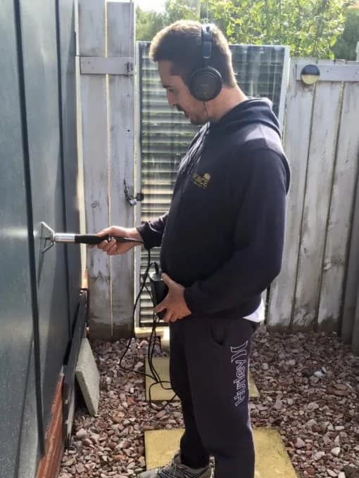 Dustin using acoustic leak-detection gear next to a Rinnai hot water unit